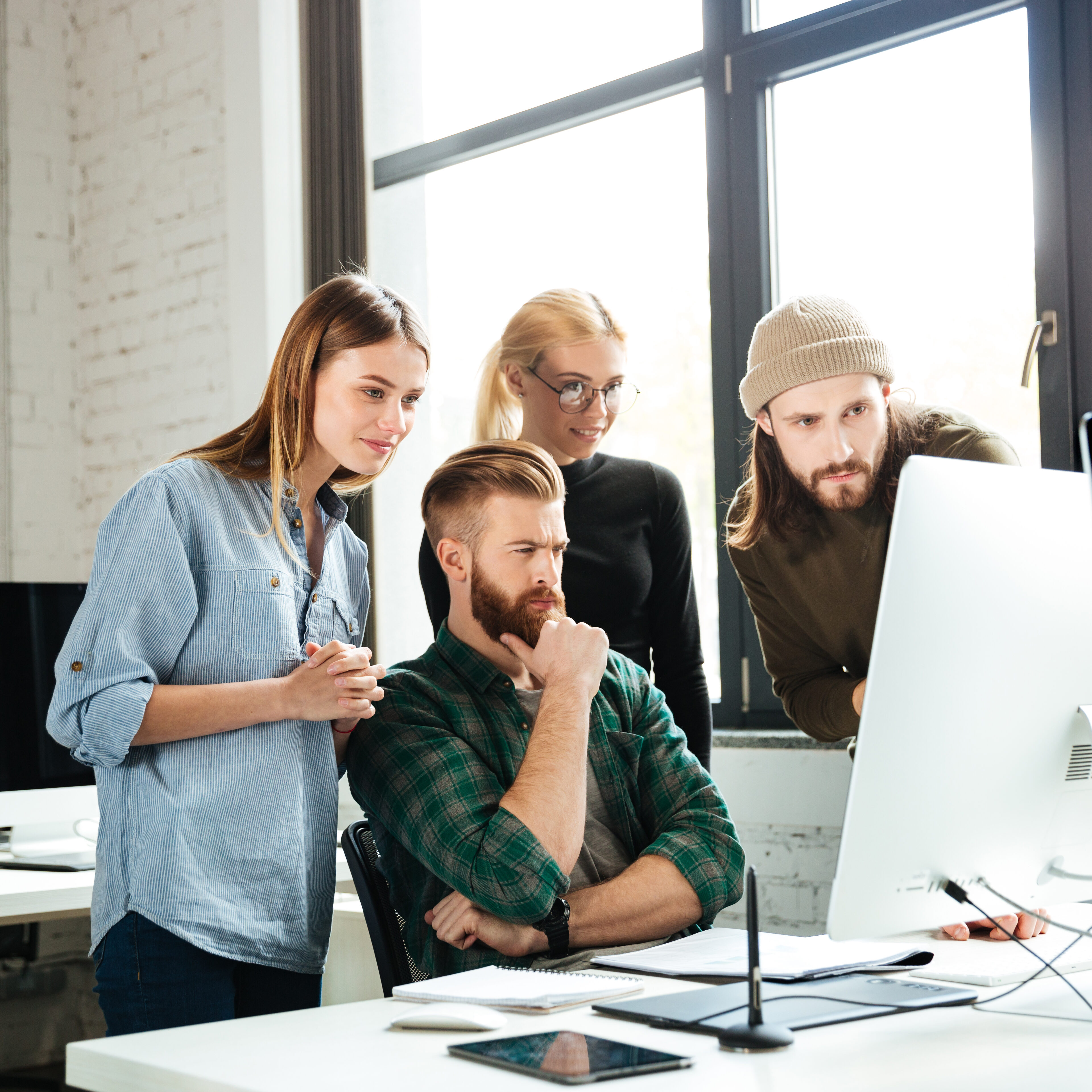 Photo of young serious colleagues in office talking with each other using computer. Looking aside.